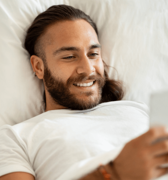 happy-young-long-haired-man-lying-in-bed-using-sm-2023-09-29-16-19-32-utc (1)